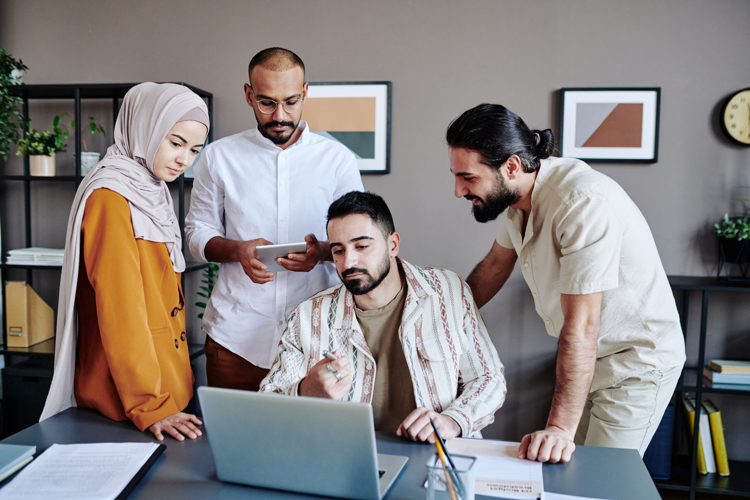 Young confident businessman pointing at data on laptop screen while making presentation for colleagues at working meeting